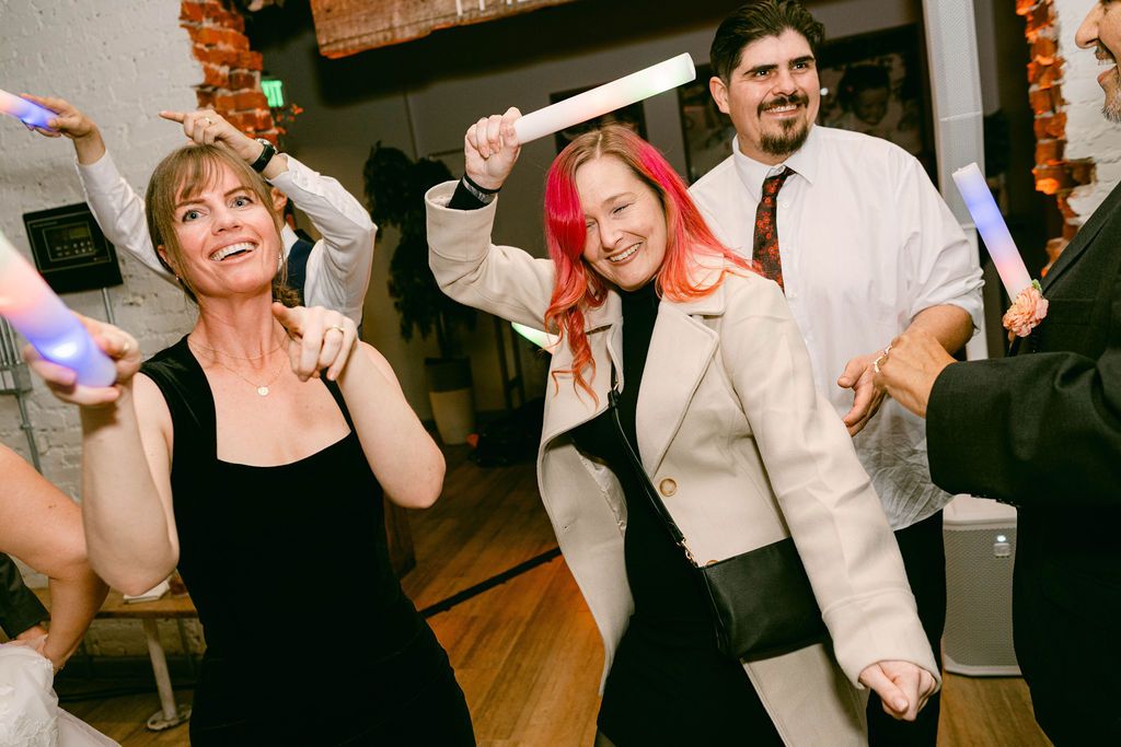 People dancing and celebrating at a lively wedding reception on a wooden dance floor.