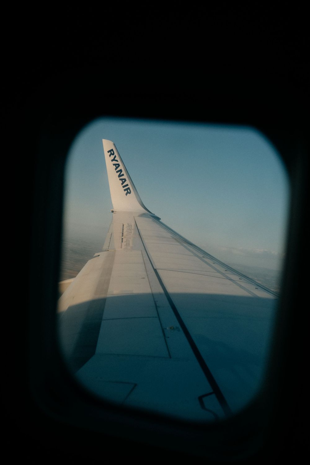 View of Ryanair airplane wing through passenger window during flight over clouds.