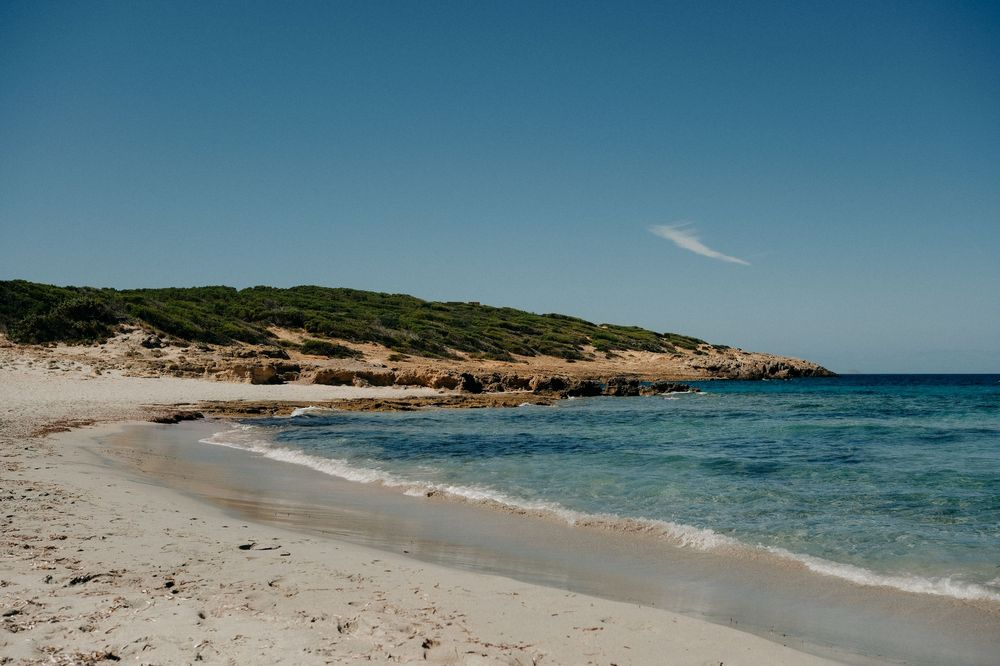 Pristine Mediterranean beach with turquoise water and sandy shoreline bordered by green hills.
