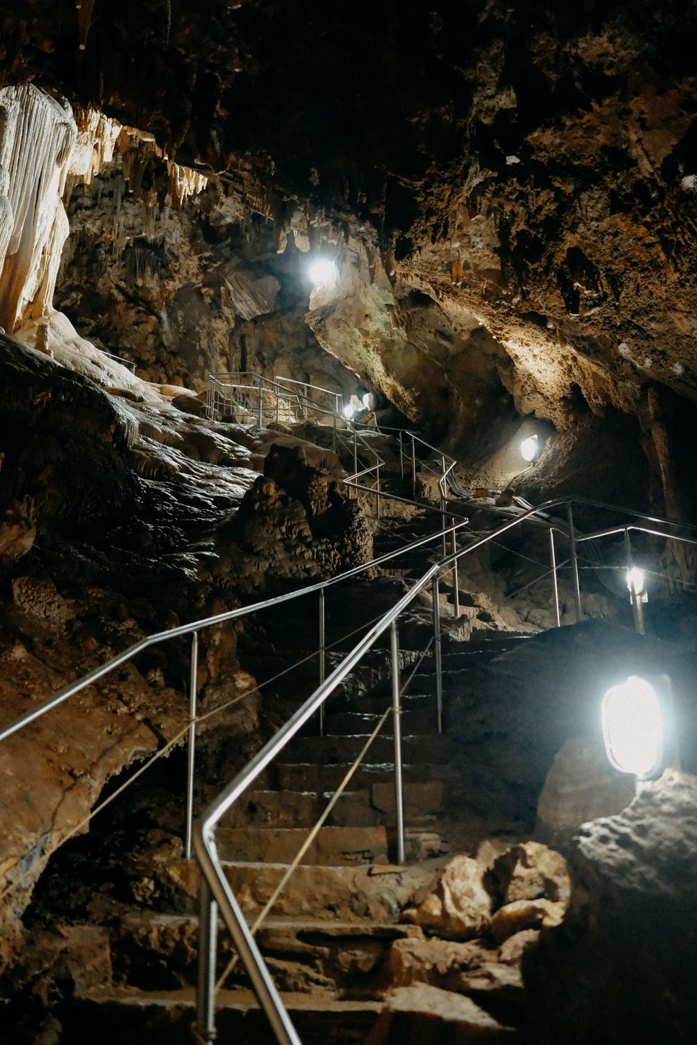 Dimly lit cave interior with metal handrails and spotlights illuminating the rocky walls.