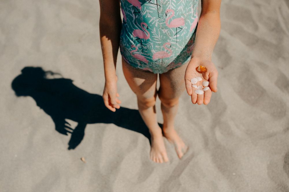 Someone wearing a turquoise floral dress holds small seashells in their hands while standing on sandy beach.