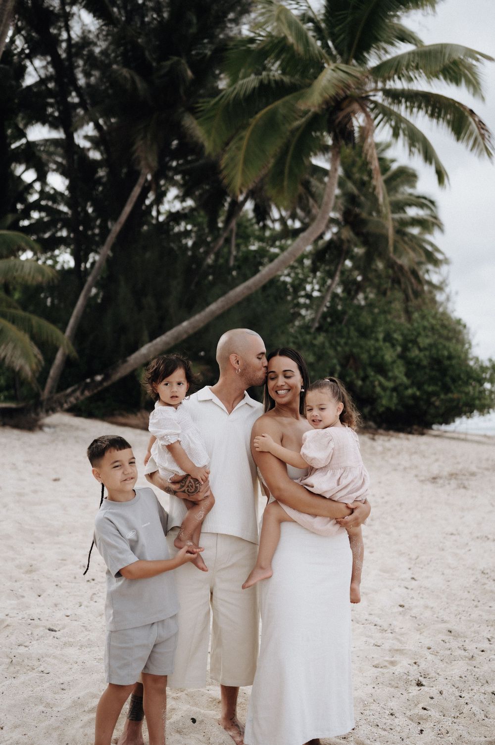 A family shares joyful moments together on a tropical beach with palm trees swaying in the background.