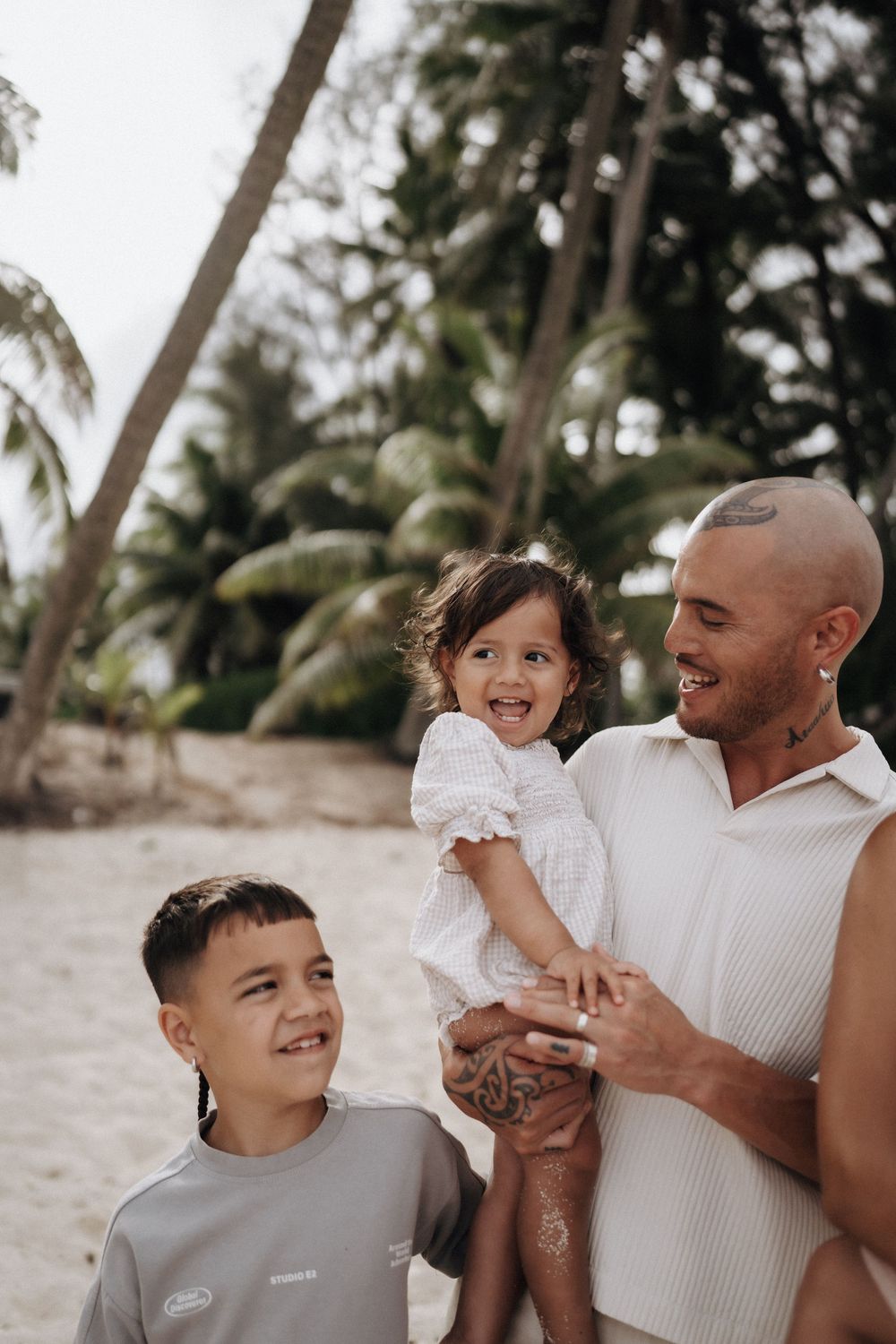 Family shares joyful moments together while playing and laughing on a tropical beach with palm trees.