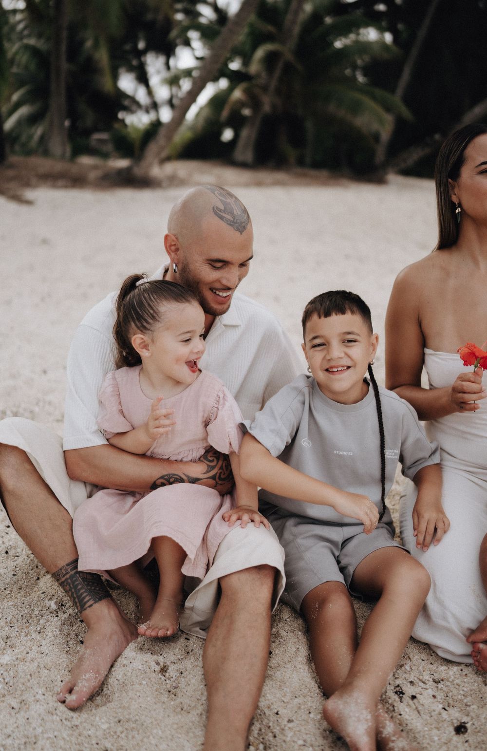 A joyful family moment captured on a beach with everyone wearing casual white and beige clothing.