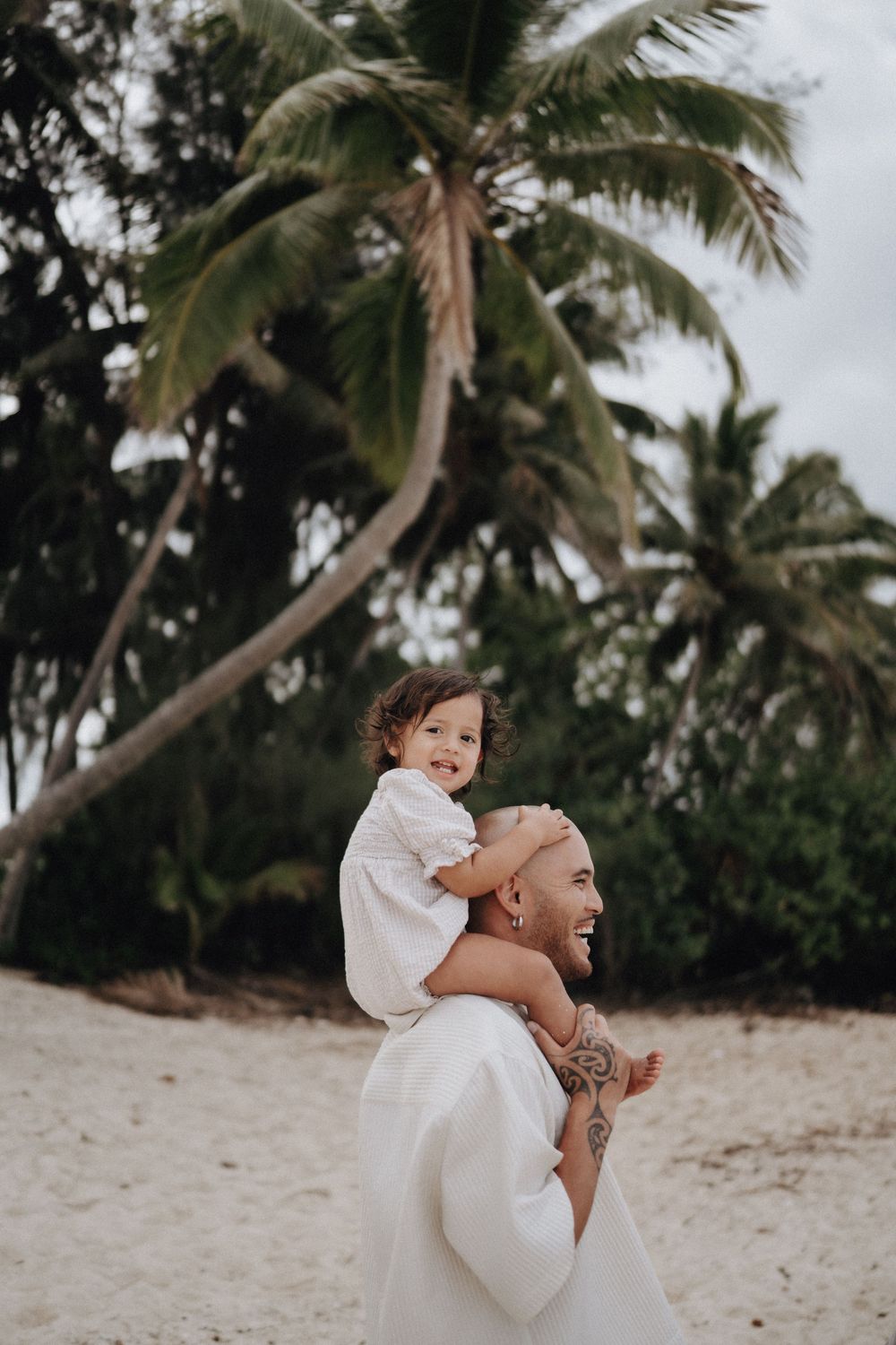 A playful moment between family members on a tropical beach with palm trees in the background.