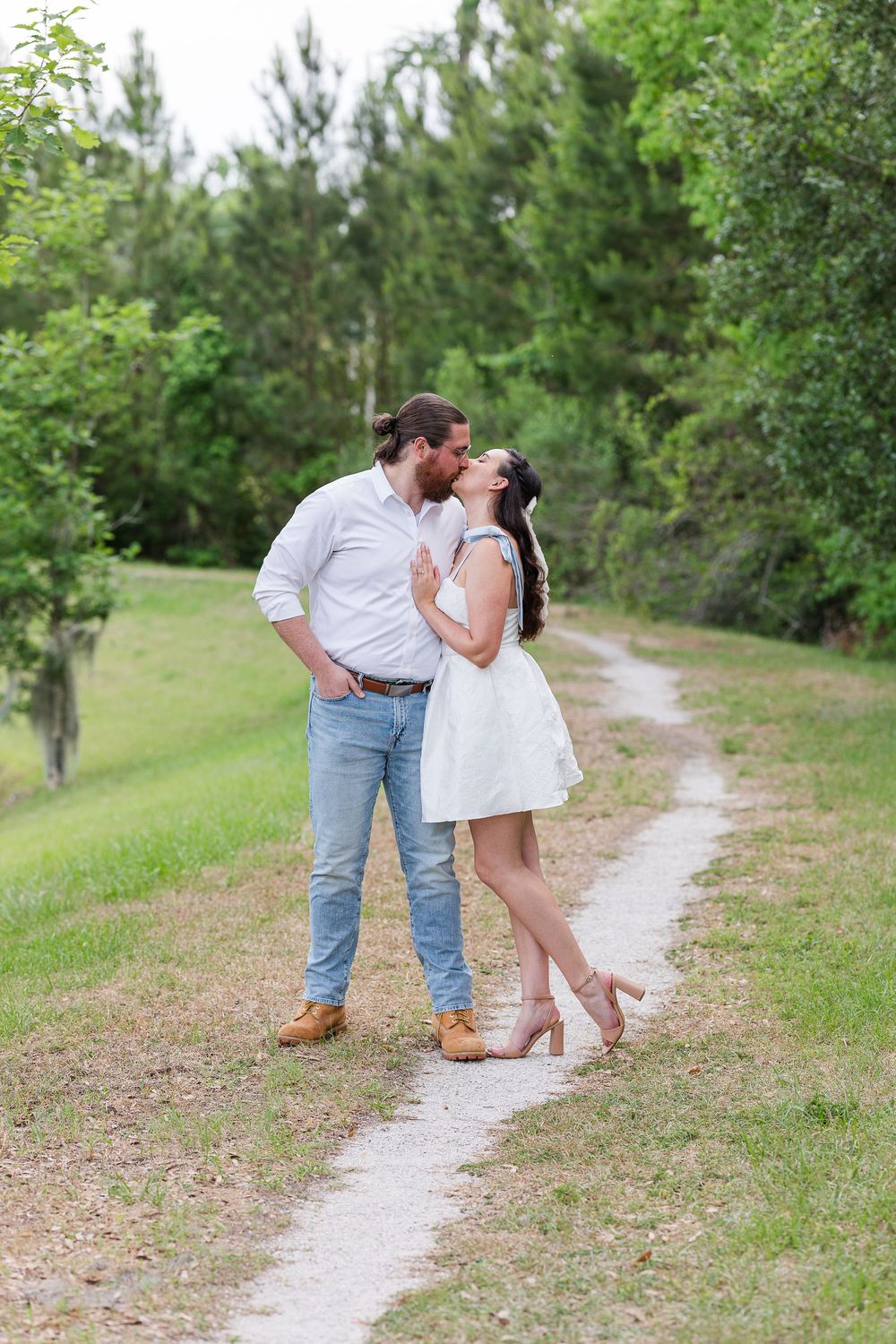 Two people in casual attire embrace on a winding path through green trees and grass.