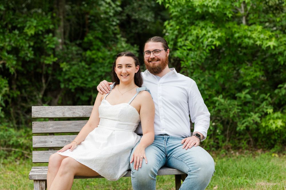 A couple shares tender moments while sitting together on a bench surrounded by lush greenery.