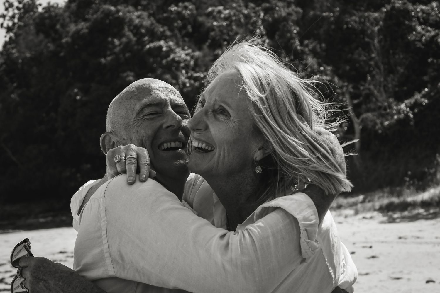 A black and white photo collage showing joyful moments of a couple embracing and laughing together outdoors.