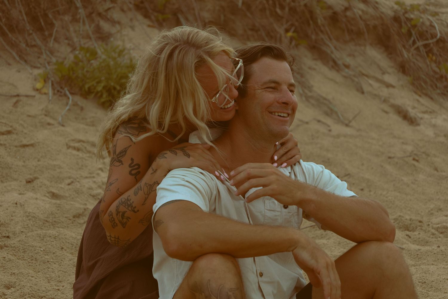 A couple shares a joyful moment together on a sandy beach at sunset.