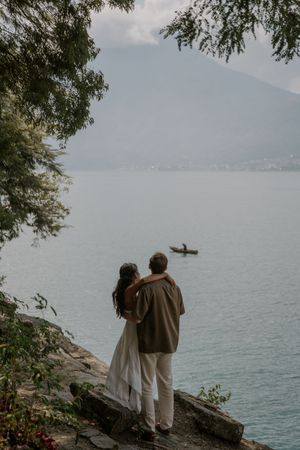 A couple stands on a rocky overlook watching a kayaker on a misty mountain lake.