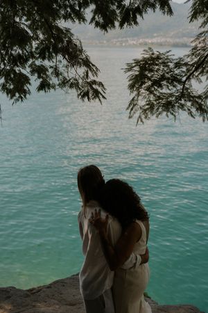 A couple sits by a turquoise lake surrounded by lush trees on a romantic afternoon.