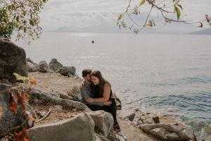 A couple sits together on rocky coastal cliffs overlooking the ocean at sunset.