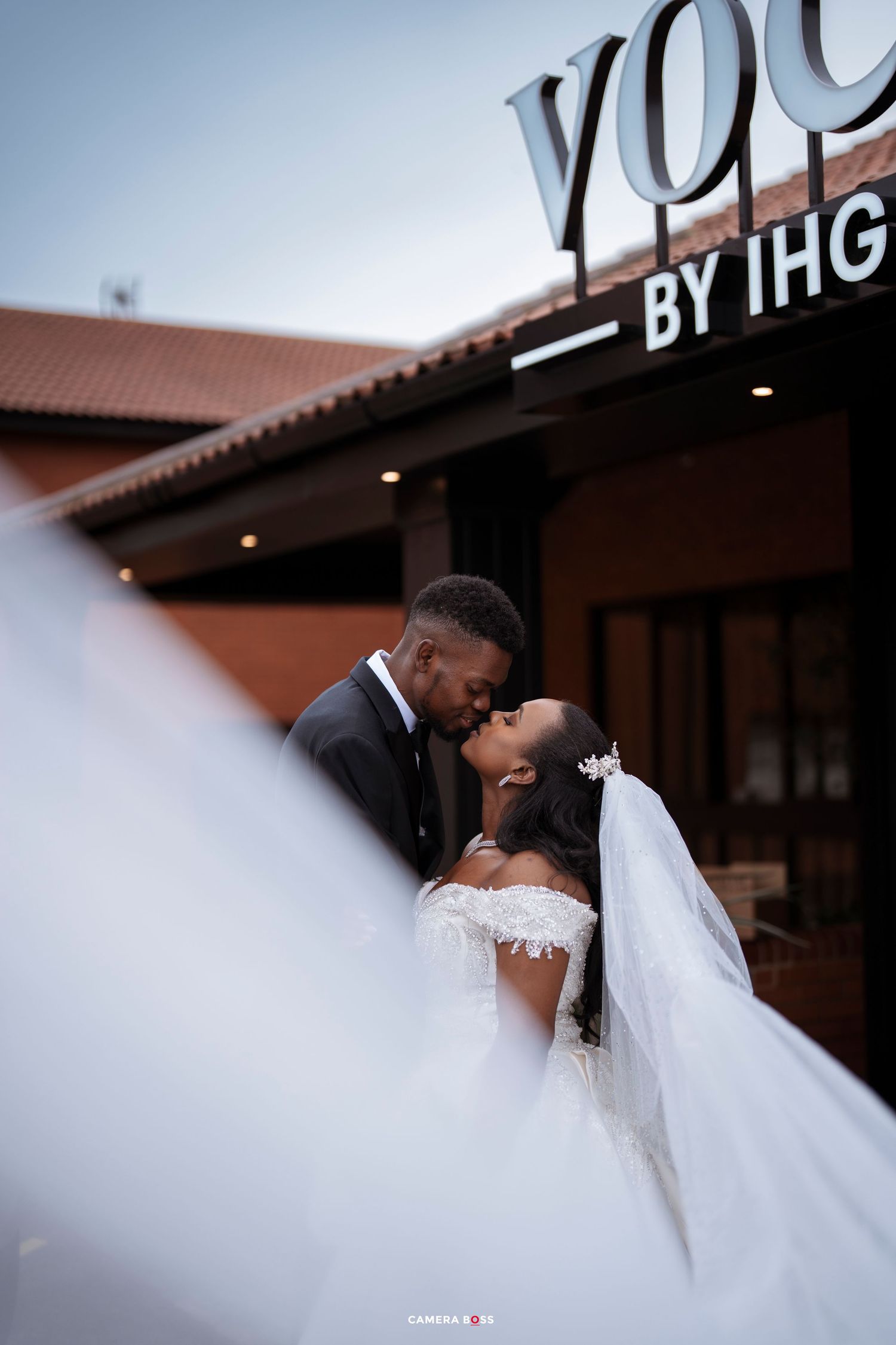 A bride and groom share a romantic kiss outside a Yoo by IHG hotel, with her white veil flowing in the breeze.