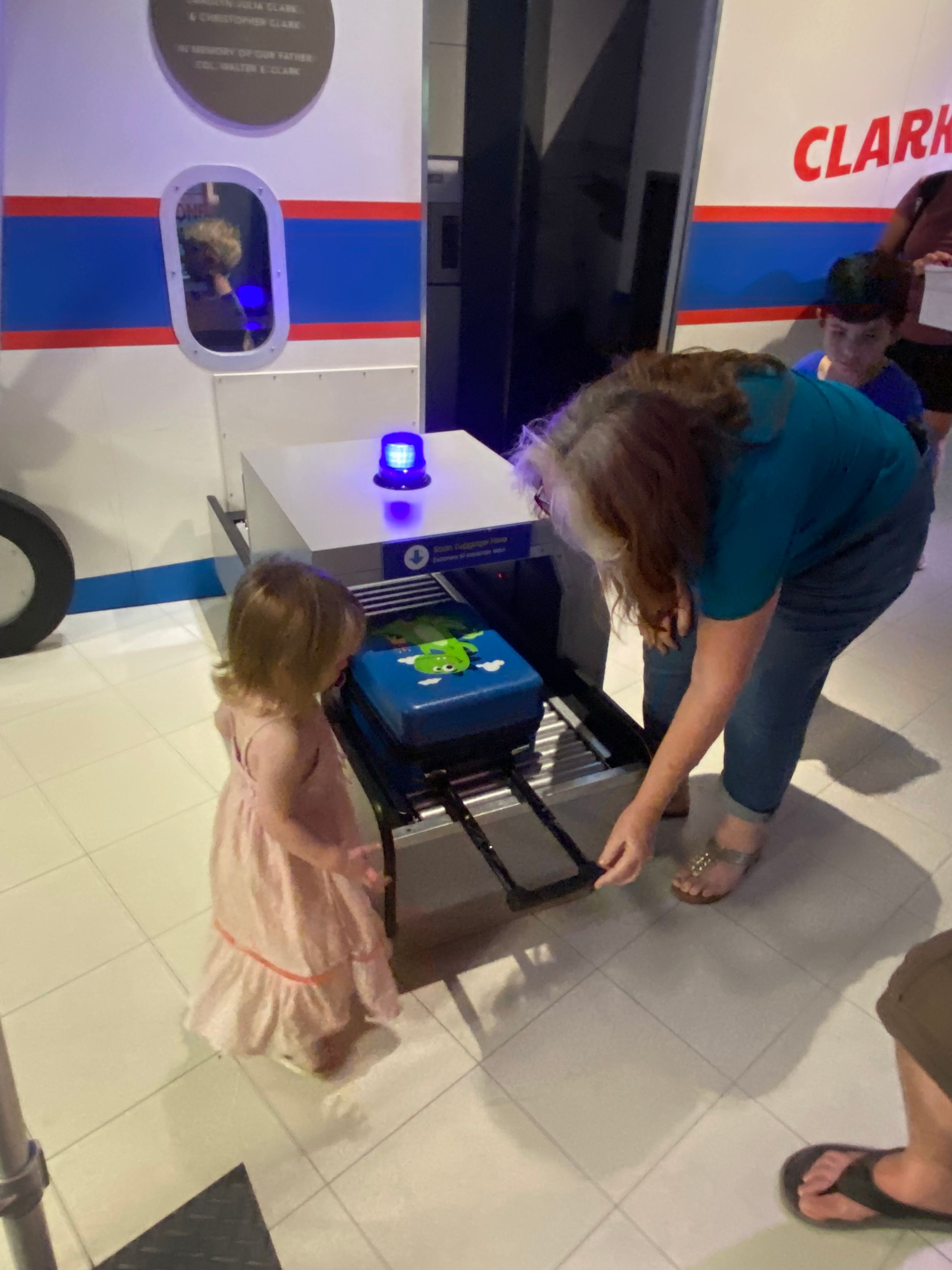 Woman and young girl exploring an interactive airport security scanner exhibit at a children's science museum.