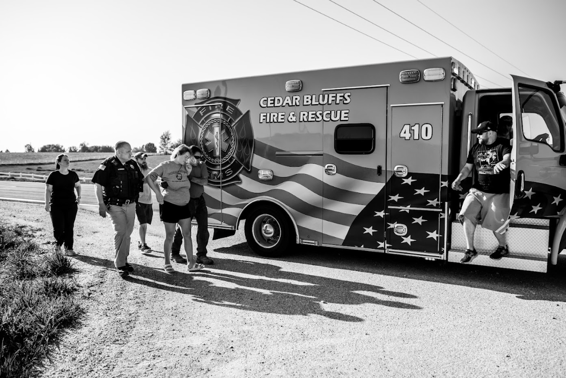 A group of people stand next to a decorated food truck with American flag design parked on a dirt road.