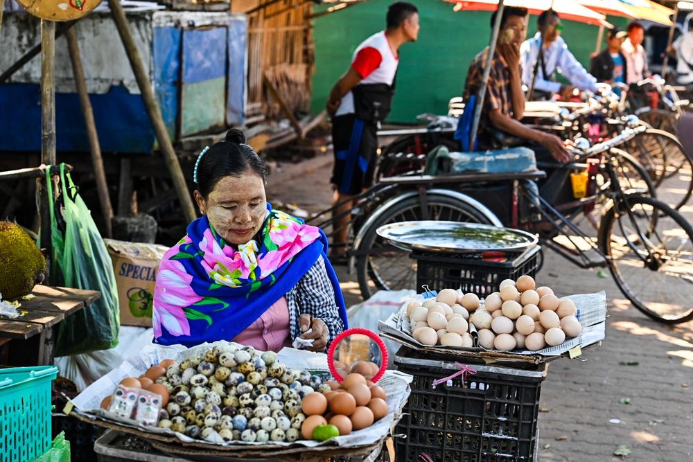 Woman selling eggs and snails at a colorful outdoor market stall in Southeast Asia.