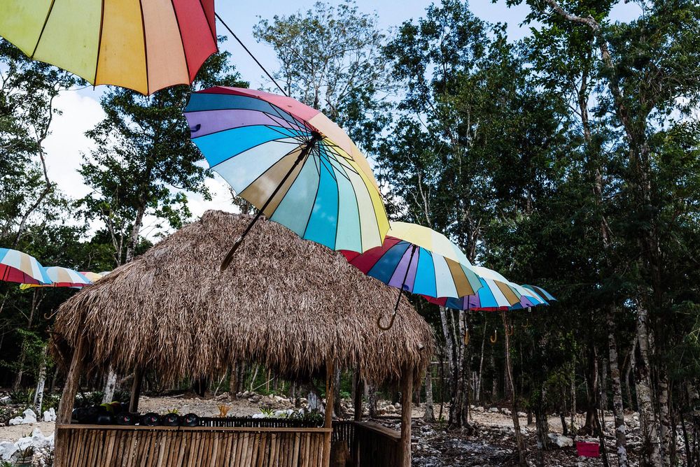 Colorful rainbow umbrellas and a thatched palapa hut in a tropical jungle setting.