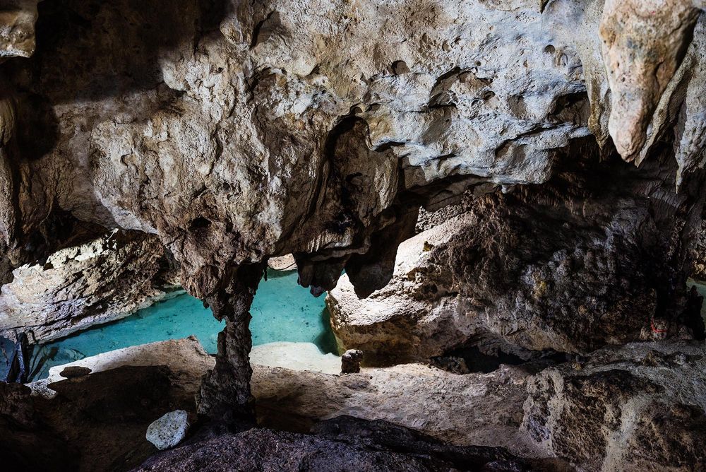Stunning cave grotto with turquoise water visible through rocky limestone arch opening in a natural cavern.