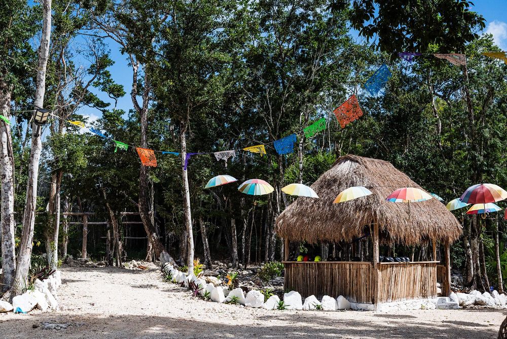 Thatched palapa hut with rainbow umbrellas and colorful bunting flags in a tropical forest.
