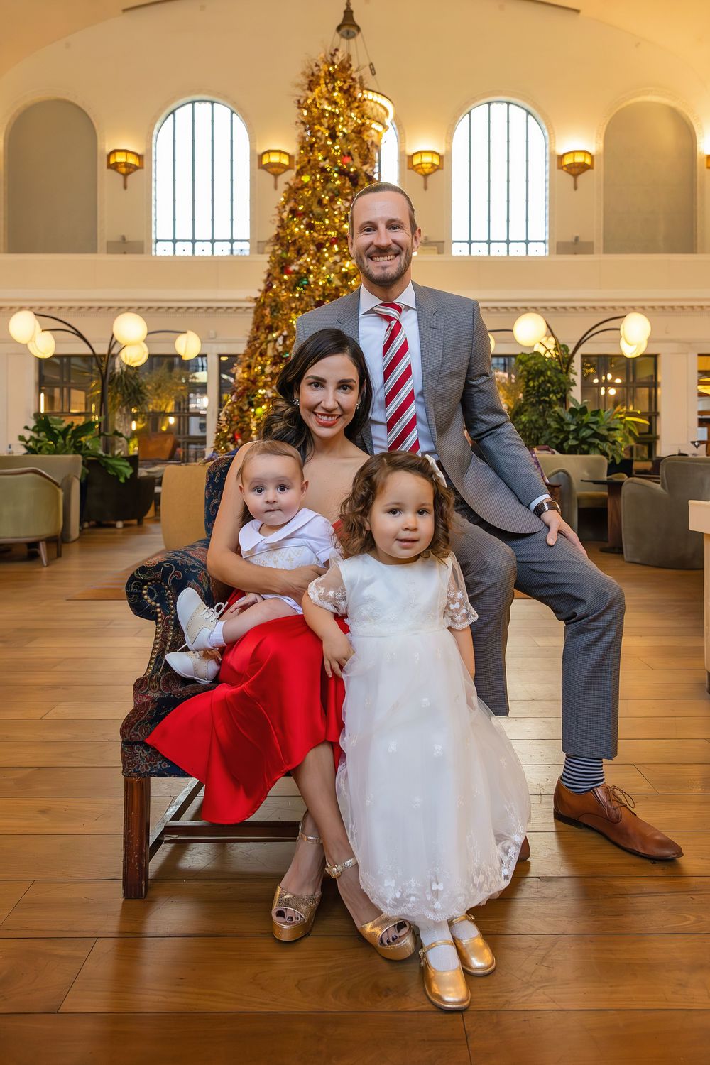 Elegant family of four posing near decorated Christmas tree in grand hall.