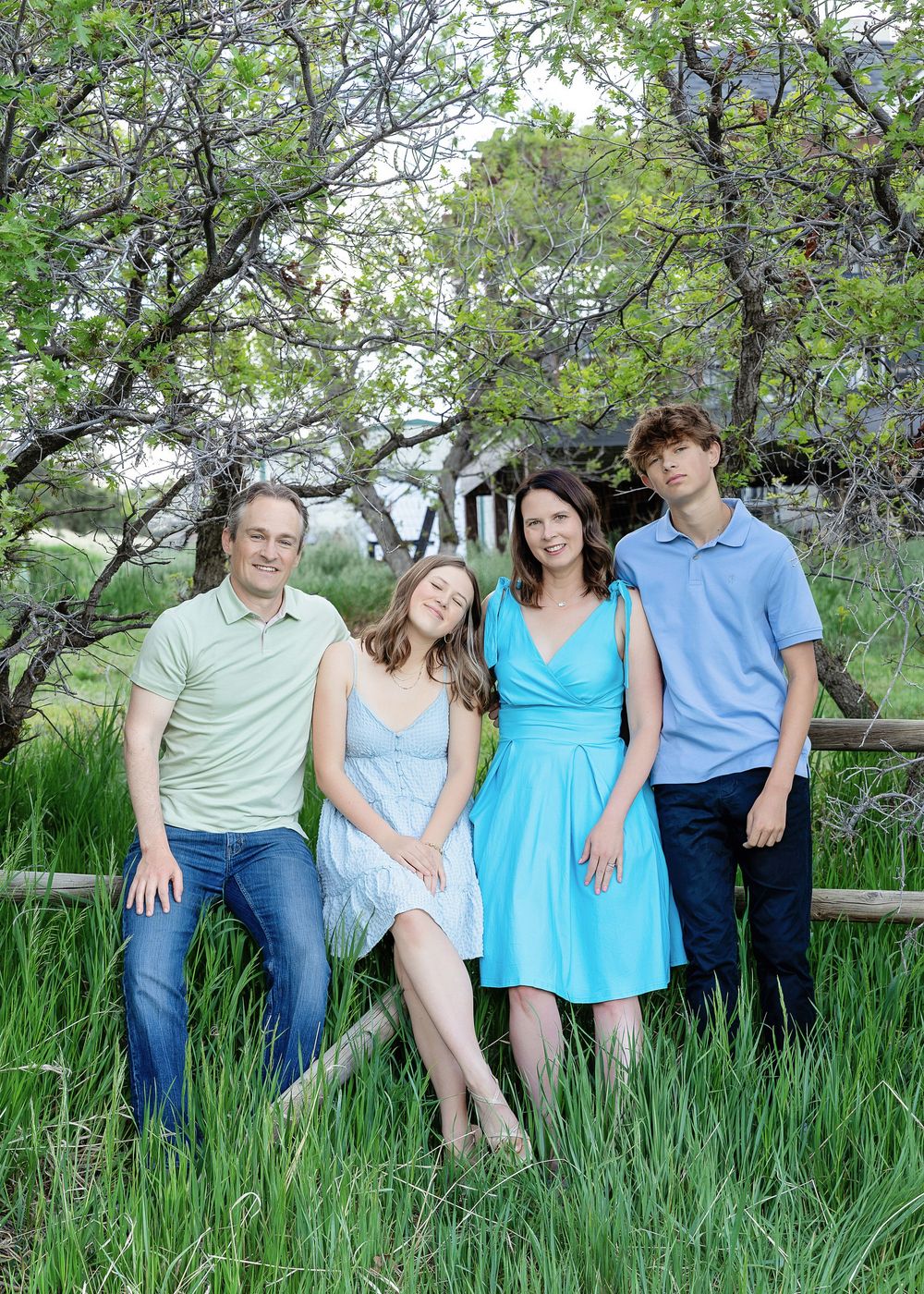 Family of four posing near rustic fence in lush green meadow.