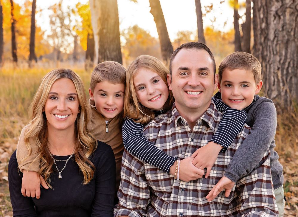 Family of five smiling outdoors among golden autumn trees.