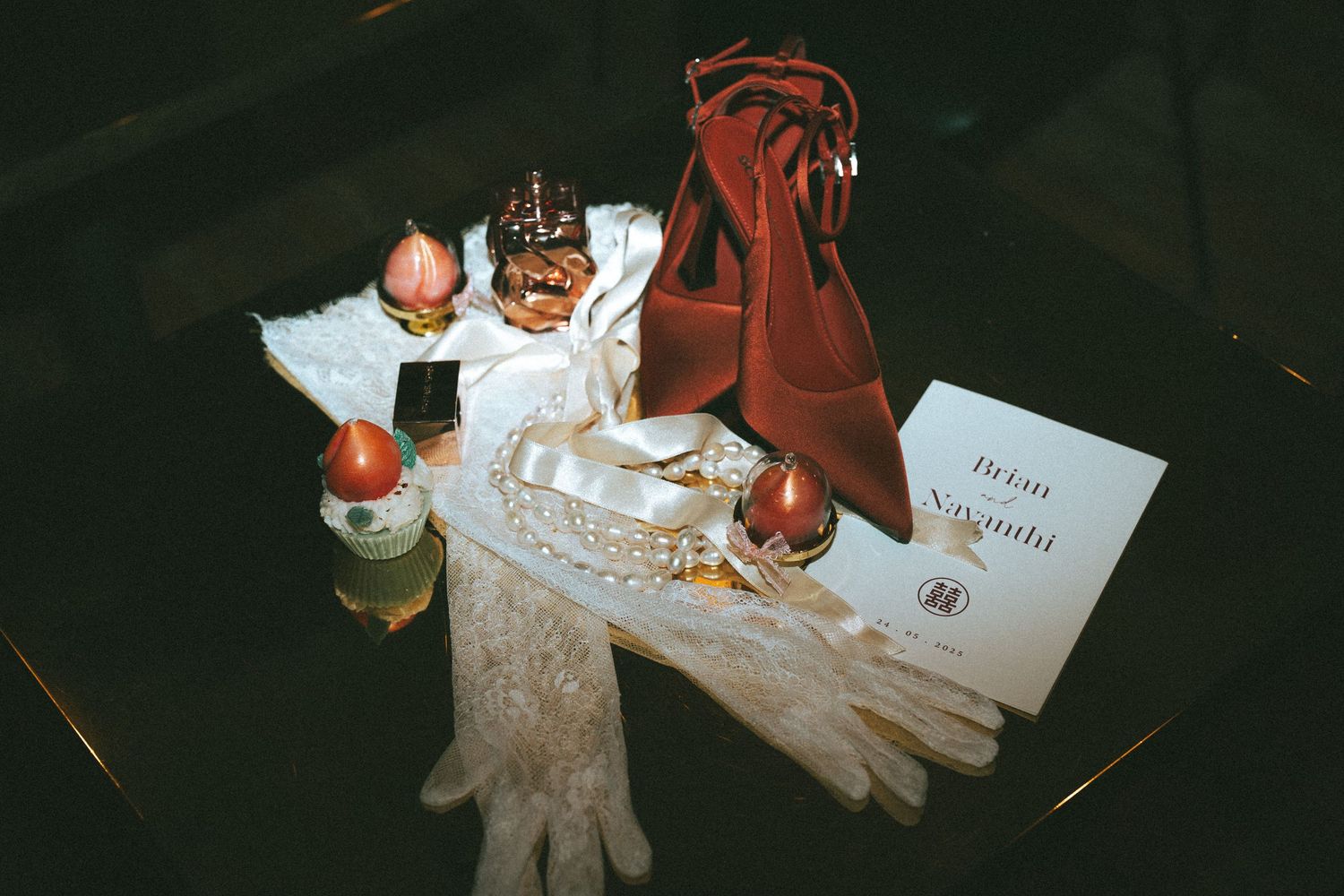Elegant flat lay of vintage accessories including lace gloves, crown, candles, red velvet bag, and an invitation card.