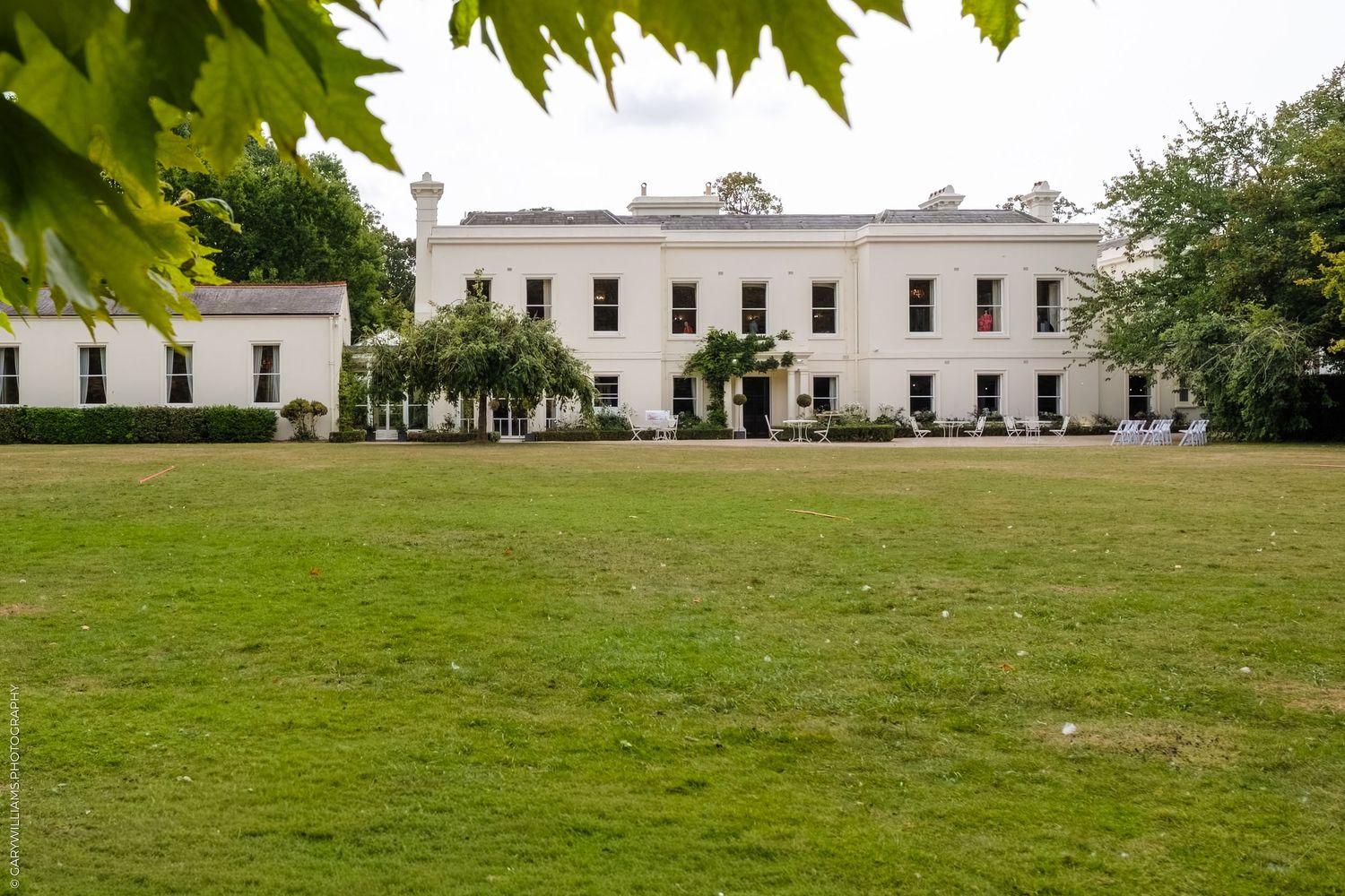 Large white Georgian manor house with expansive green lawn on a cloudy day.