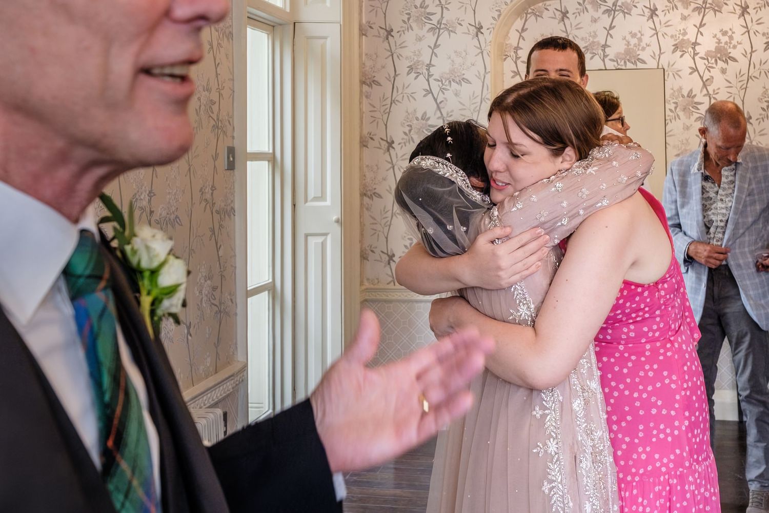 Bride and guest sharing warm hug at wedding reception indoors.