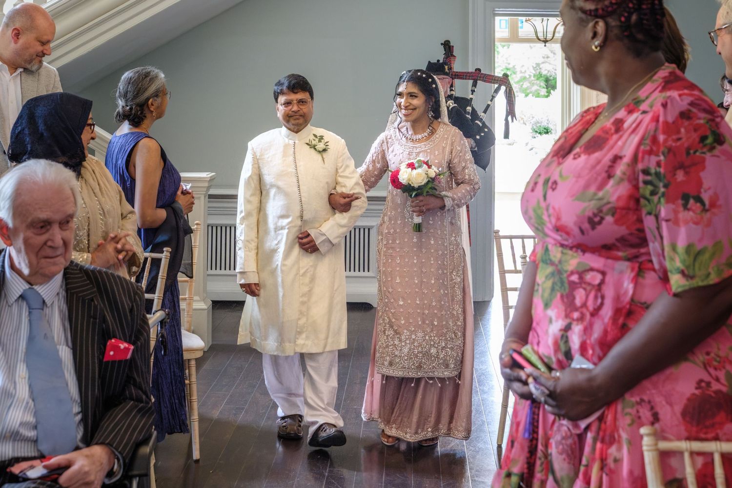 South Asian couple in traditional wedding attire walking down the aisle at indoor ceremony.