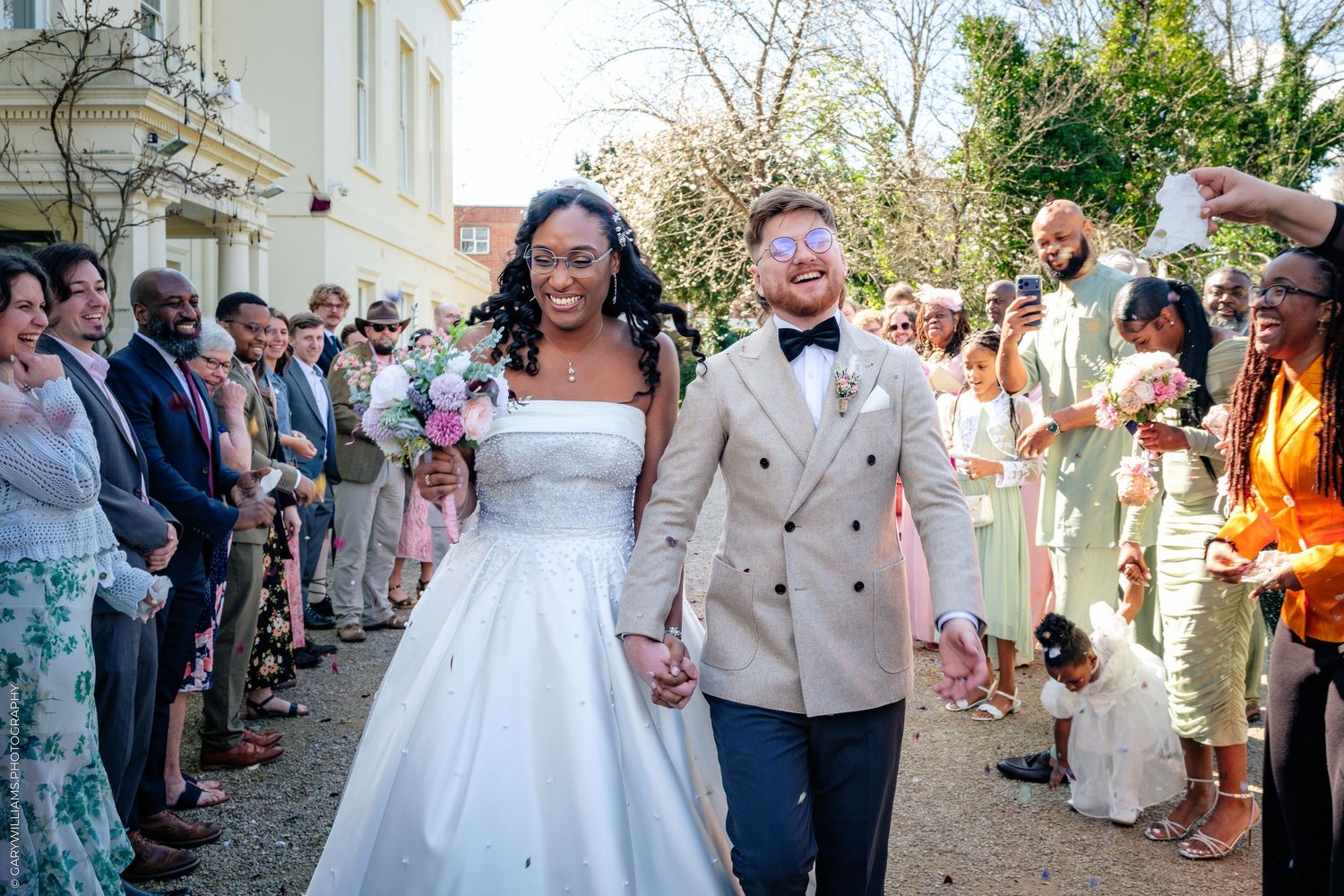 Joyful newlywed couple walking hand in hand through cheering guests at an outdoor wedding ceremony.