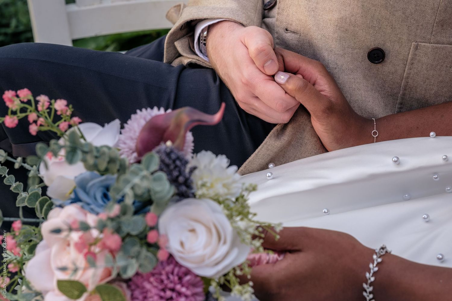 Interracial couple holding hands at wedding with colorful bridal bouquet featuring blue hydrangeas and pink roses.