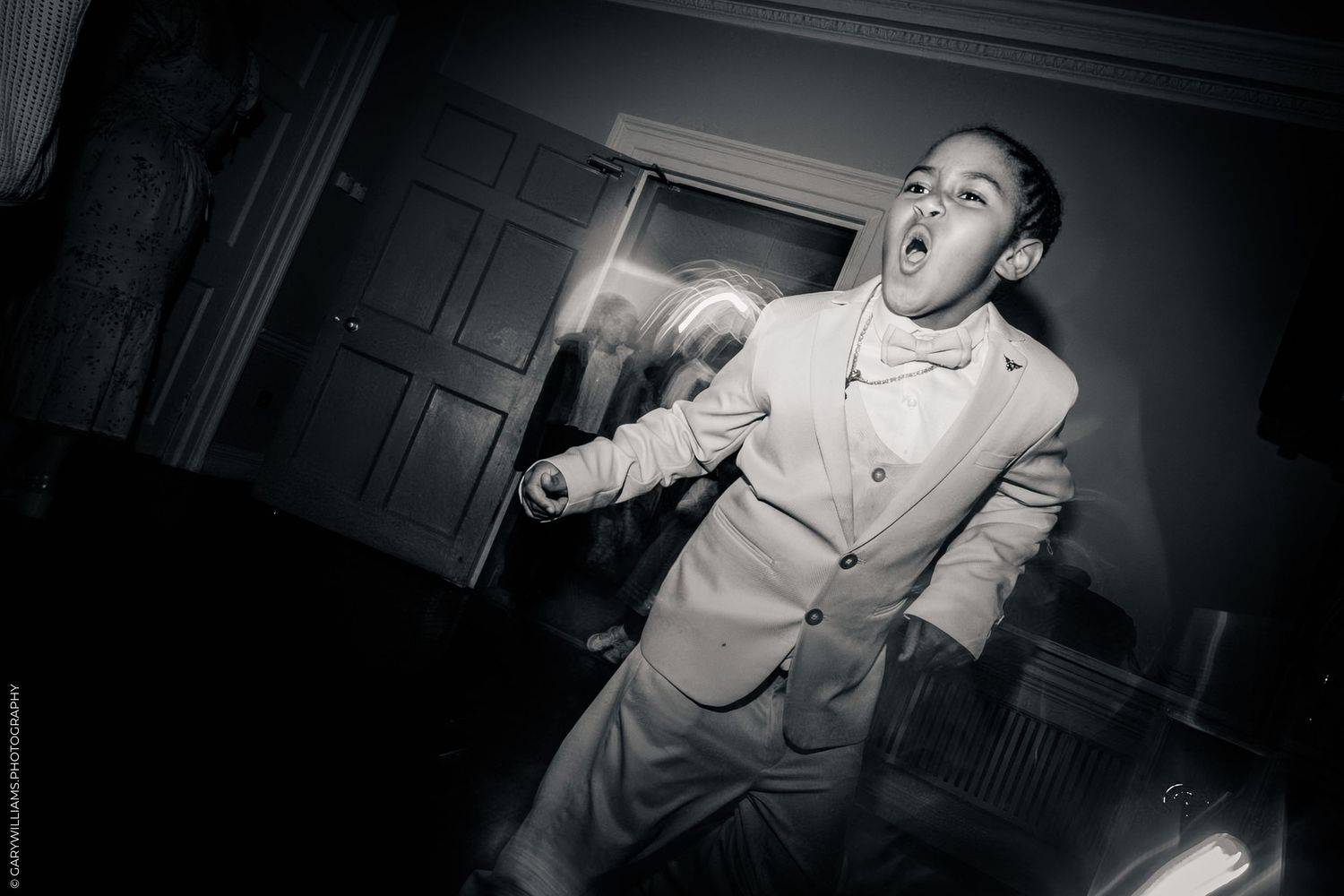 Black and white photo of a young boy in a suit dancing energetically at a formal event.