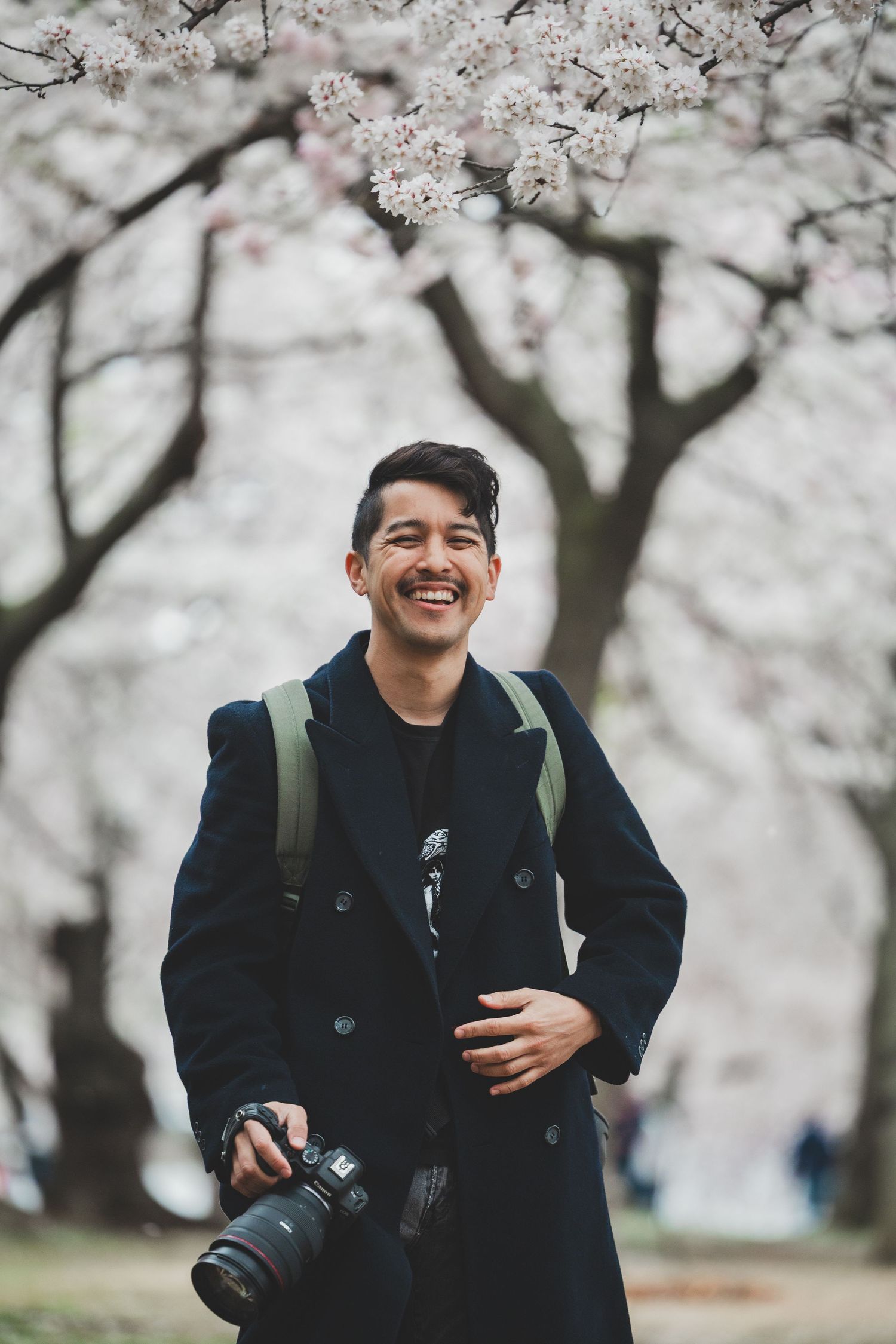 Photo of Stefan, a dc photographer, holding a camera outdoors under blooming cherry blossom trees.