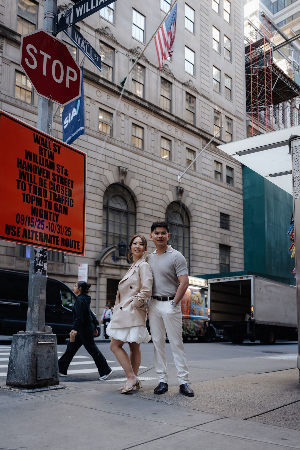 Stylish couple posing on Wall Street corner in NYC near a stop sign and street closure notice.