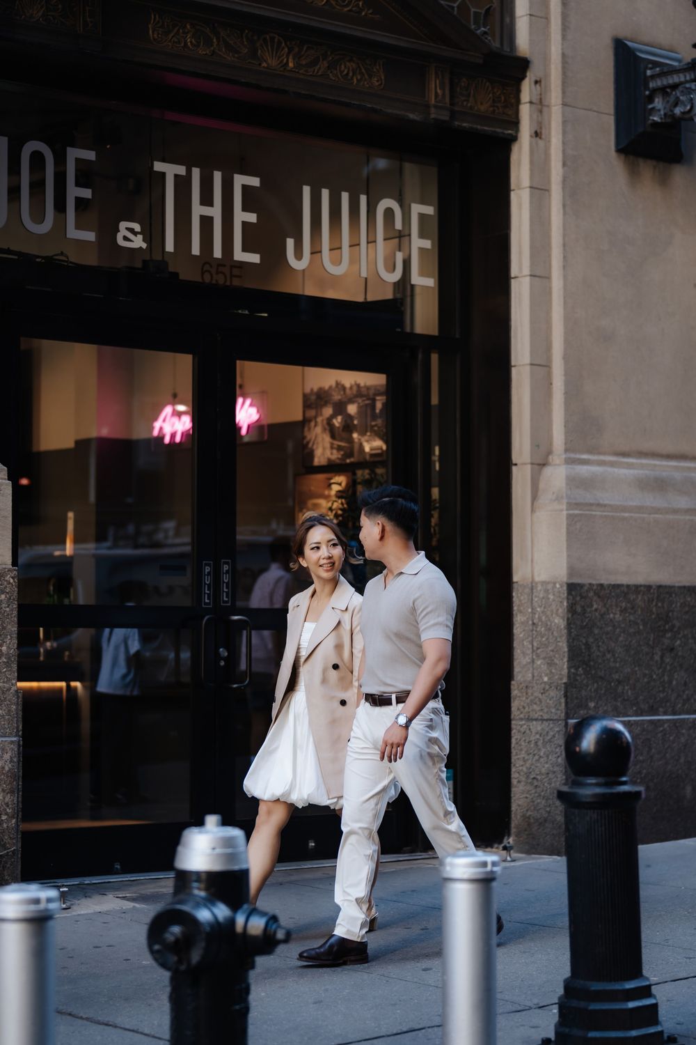 Couple in cream outfits walking past Joe & The Juice cafe on a city street.