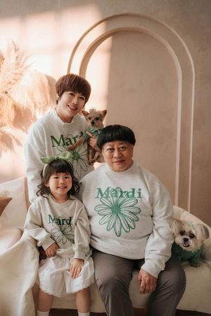 Family of three wearing matching Mardi sweatshirts pose with two small dogs in a warm studio setting.