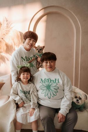 Family of three wearing matching Mardi sweatshirts pose with two small dogs in a soft beige studio setting.