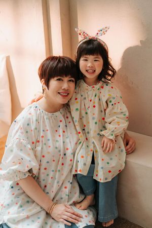 A mother and daughter in matching colorful polka dot blouses smile together, the girl wearing bunny ear headband.