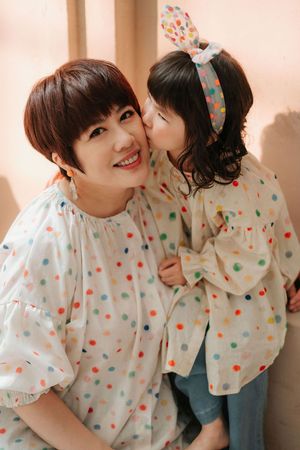 A smiling woman and young girl in matching colorful polka dot blouses, as the child kisses her cheek affectionately.
