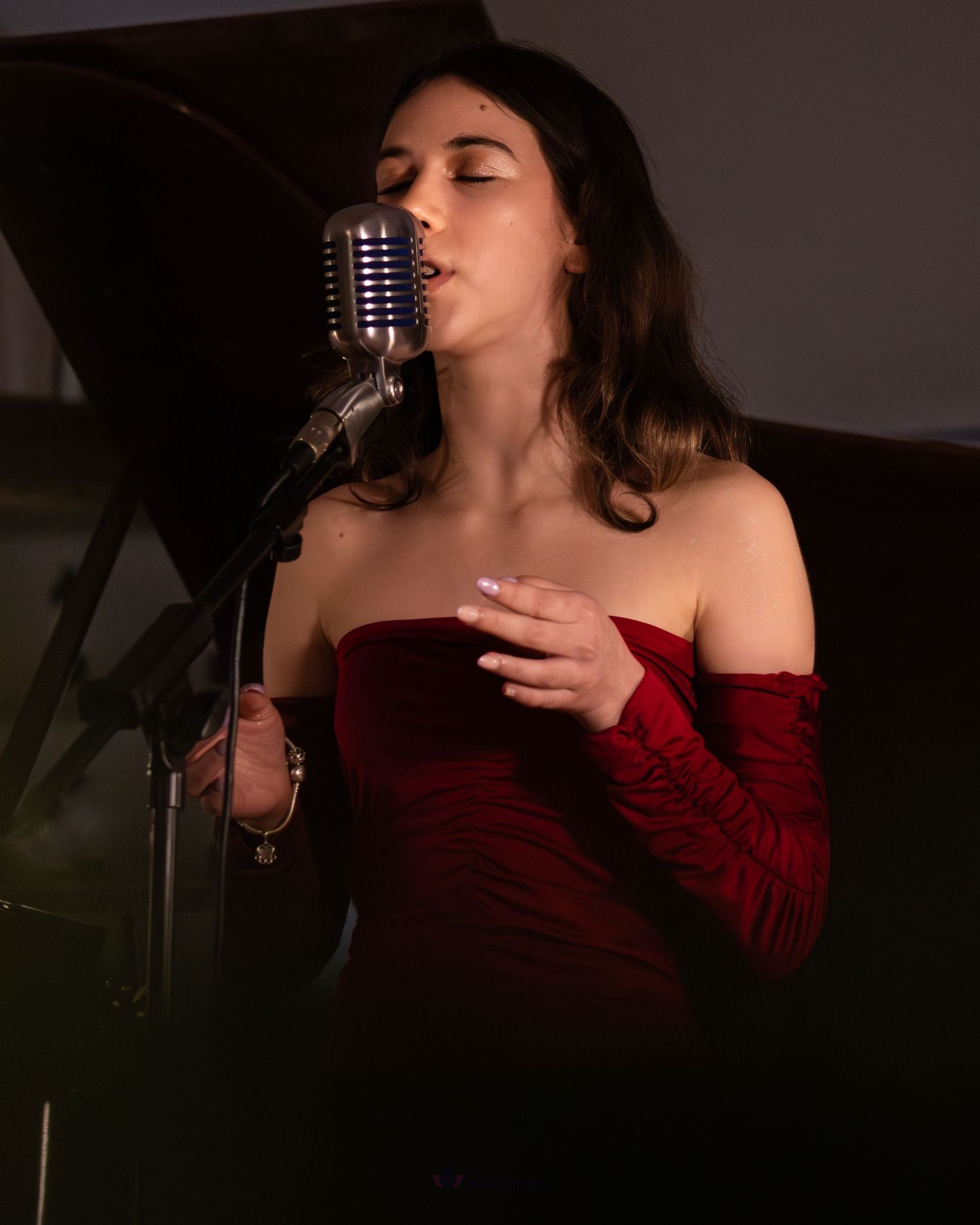 Woman in red velvet off-shoulder gown singing passionately into a vintage microphone on stage.