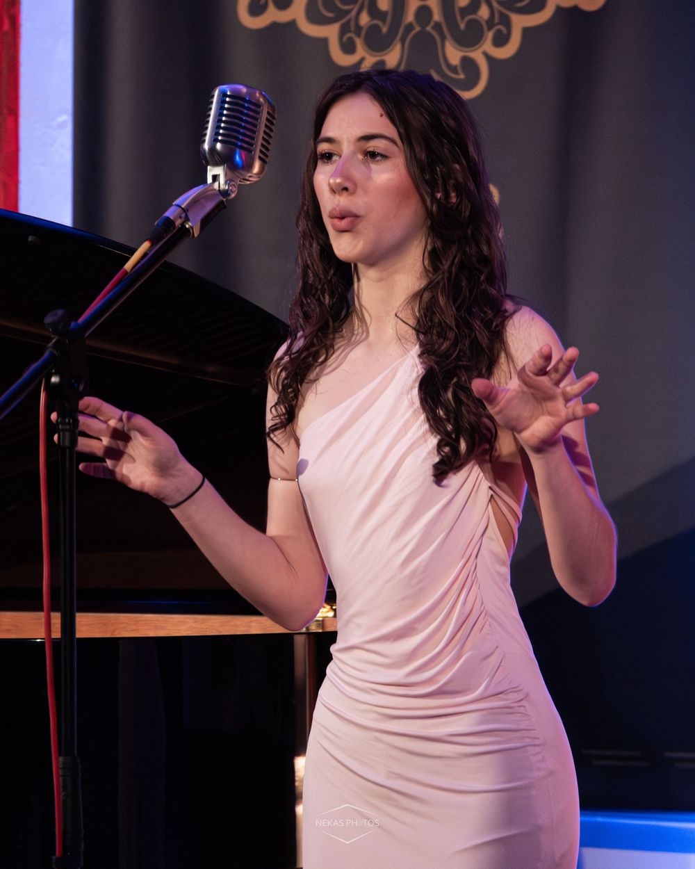 Young woman in white dress performing at vintage microphone stand on stage.