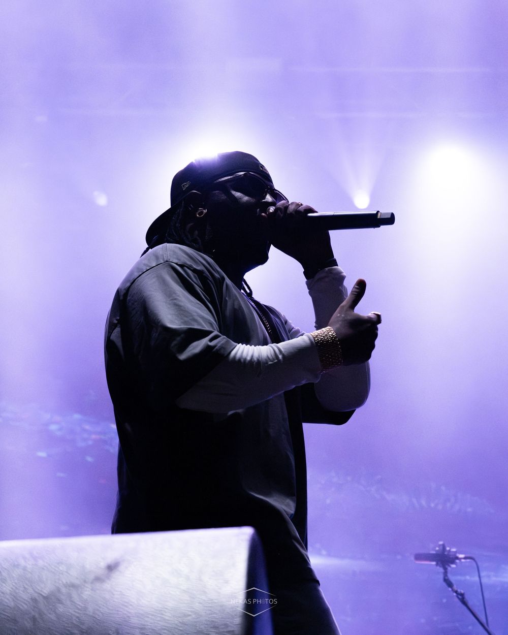 Rapper performing on stage with microphone, silhouetted against purple stage lights at a live concert.