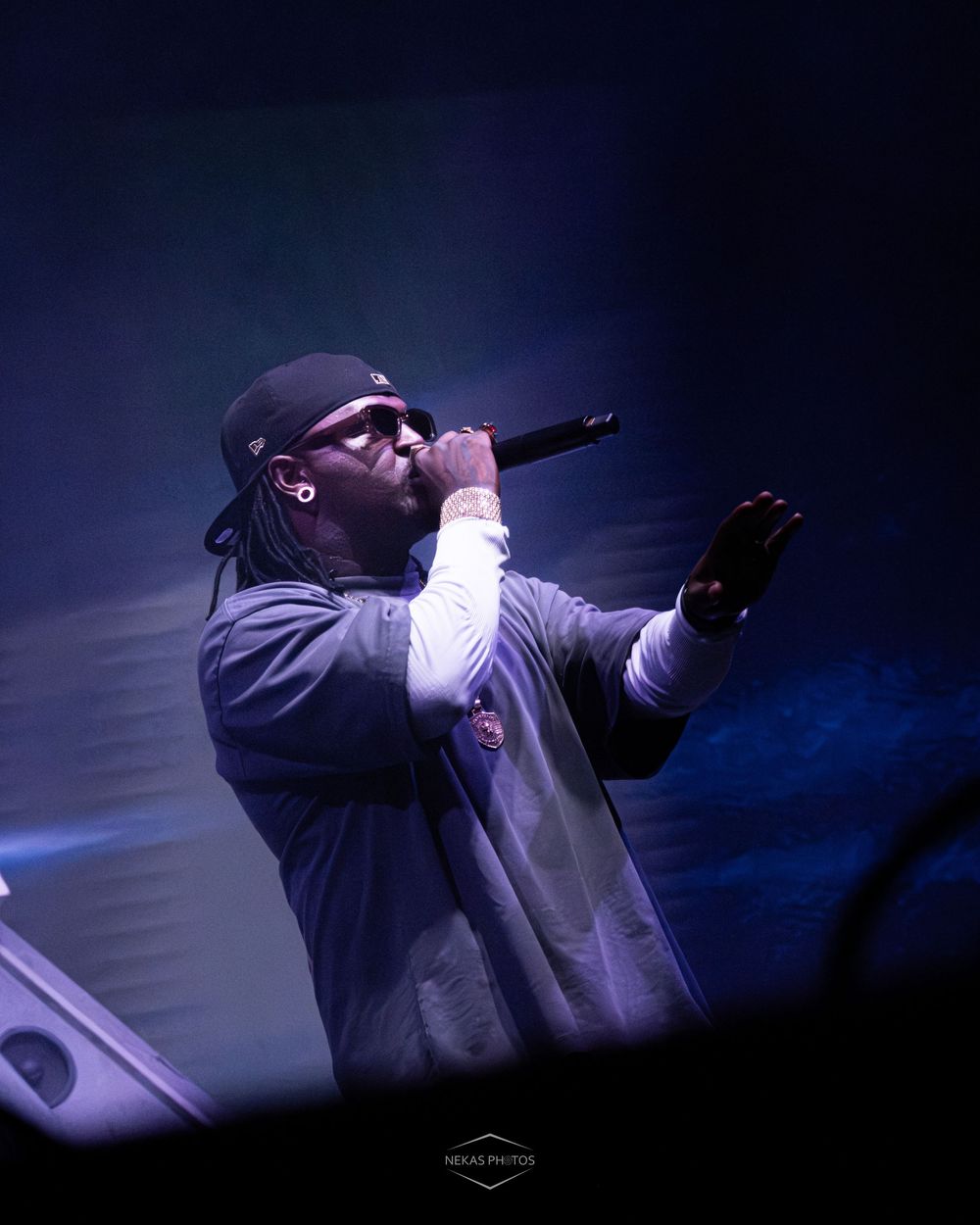 Rapper performing on stage holding microphone with blue stage lighting and smoke effects.