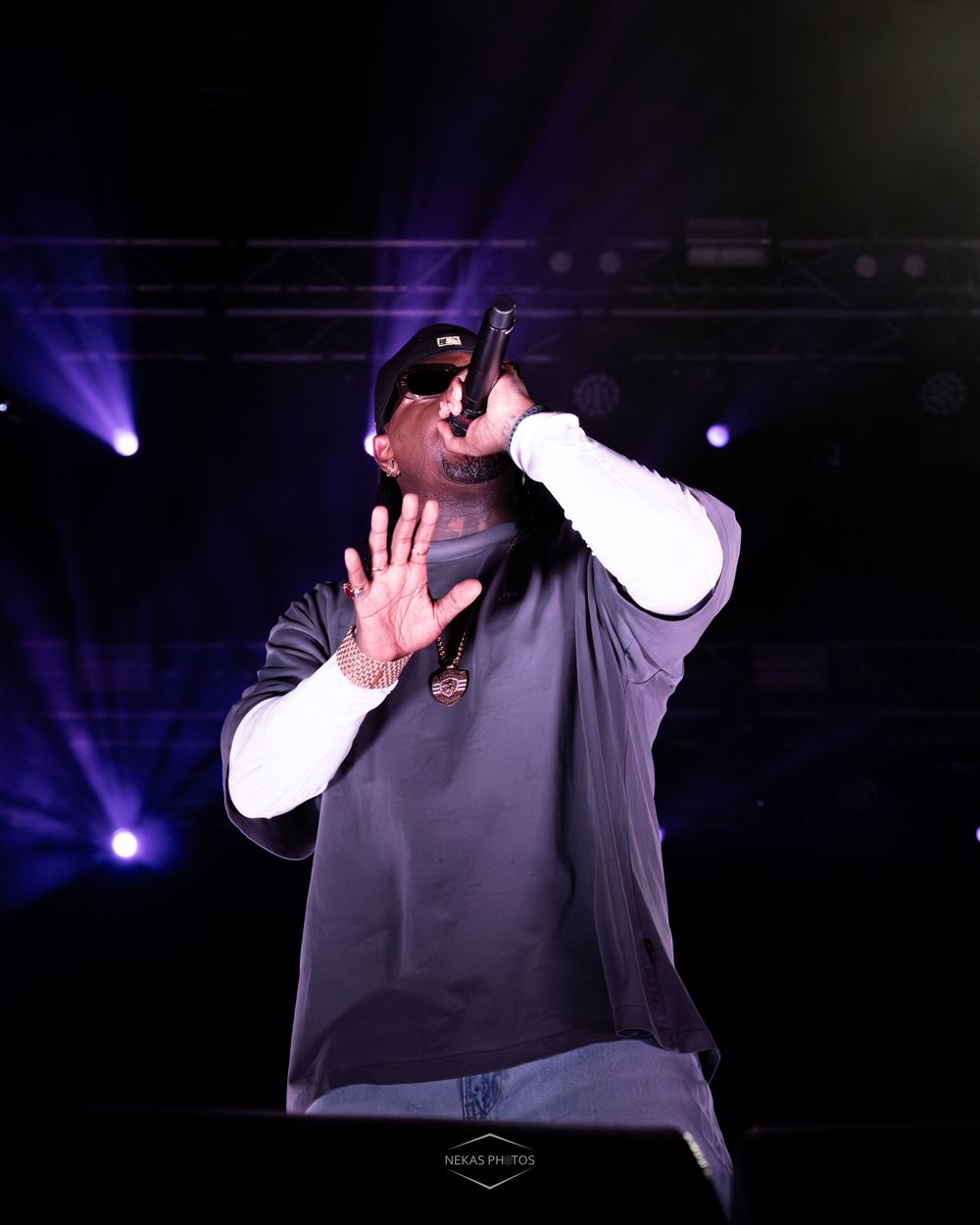 A rapper performs on stage holding a microphone under dramatic purple stage lights during a live concert.