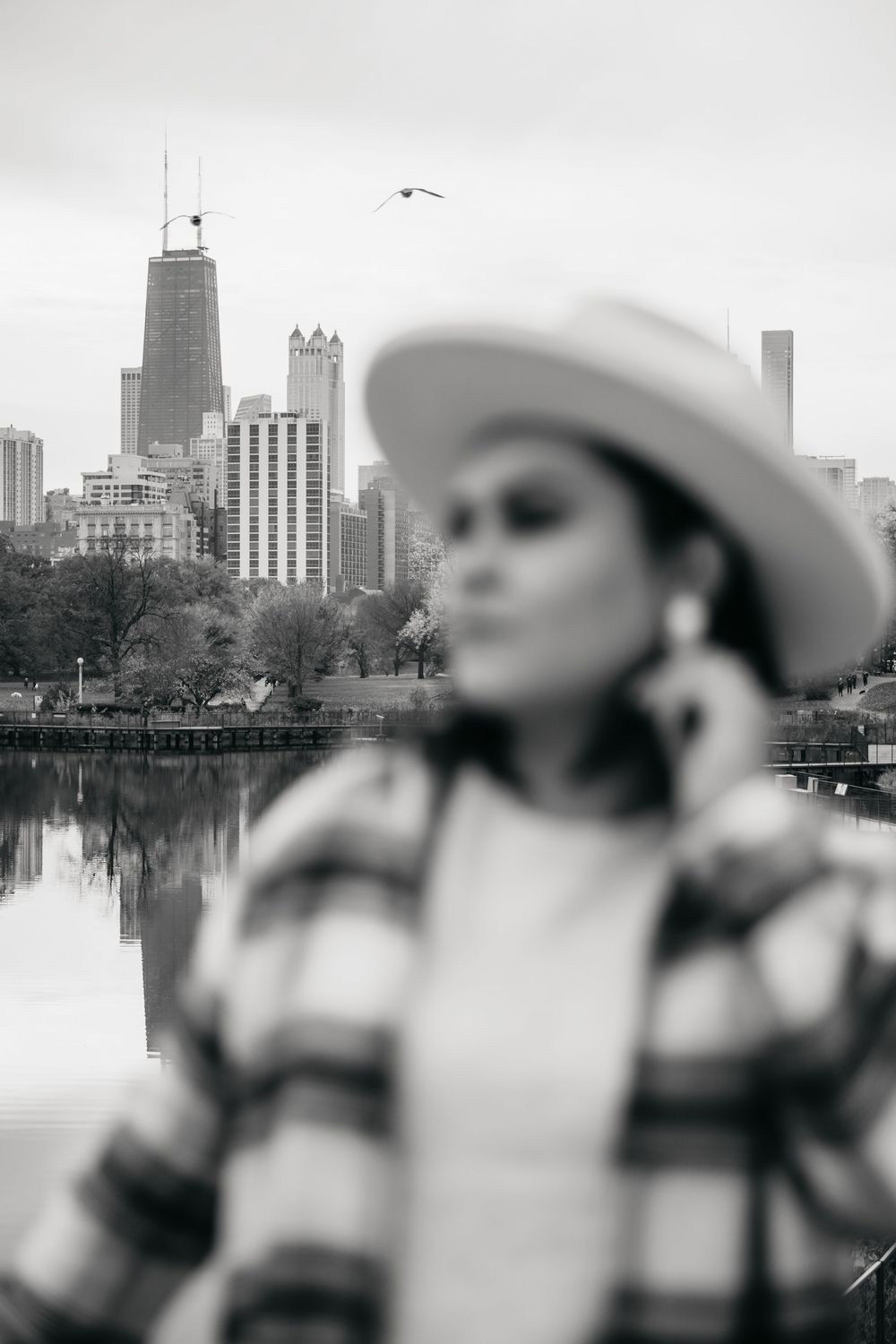 Black and white photo of a woman in a cowboy hat and plaid shirt with Chicago skyline and lake in background.