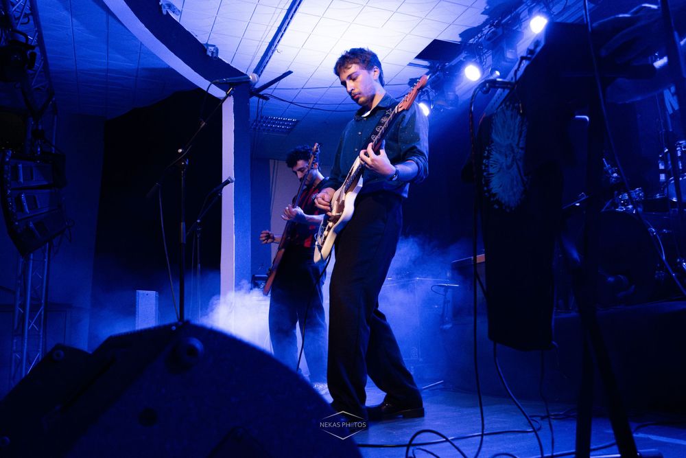 Guitarist performing on stage under blue lights with atmospheric fog at a live music concert.