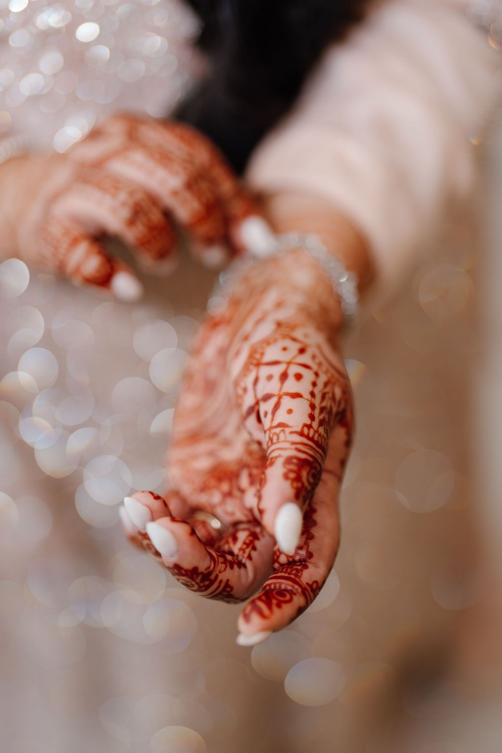 Close-up of South Asian bride's hands adorned with intricate red henna mehndi and white nail polish.