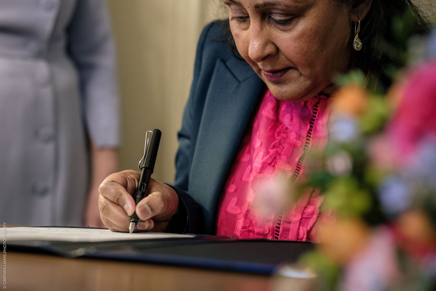 Elegant woman in pink dress signing document with fountain pen at wooden desk.