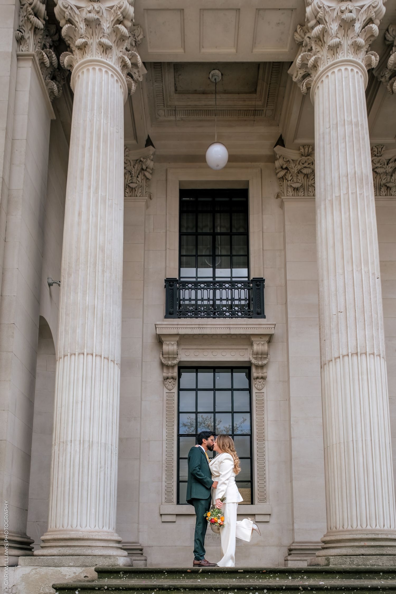 Couple sharing a kiss between grand Corinthian columns at a neoclassical building wedding venue.